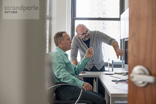 Zwei Männer in einem Büro  die auf einen Computerbildschirm schauen.