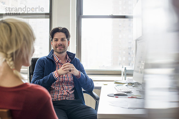 Büroalltag. Ein Mann und eine Frau in einem Büro  im Gespräch miteinander sitzend.