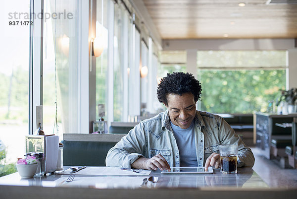 Ein Mann sitzt in einem Diner und benutzt ein digitales Tablett.