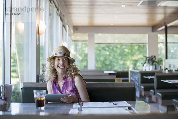 Eine Frau mit Hut  die in einem Diner sitzt und ein digitales Tablett in der Hand hält.