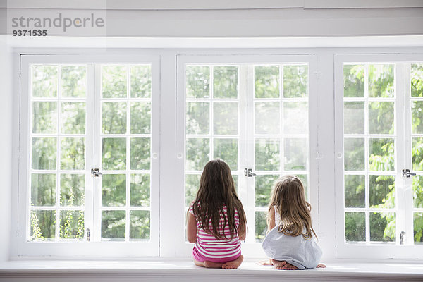 Zwei Mädchen sitzen nebeneinander an einem großen Fenster.