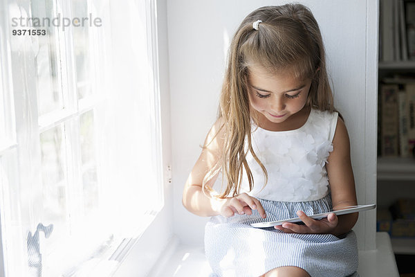 Ein junges Mädchen sitzt an einem Fensterplatz und benutzt ein digitales Tablett.