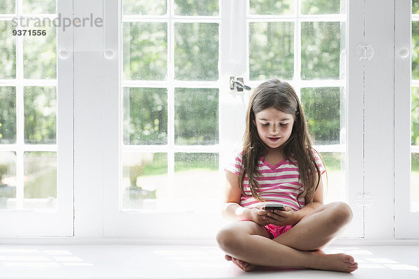 Ein Mädchen sitzt spielend mit einem Smartphone in der Hand.