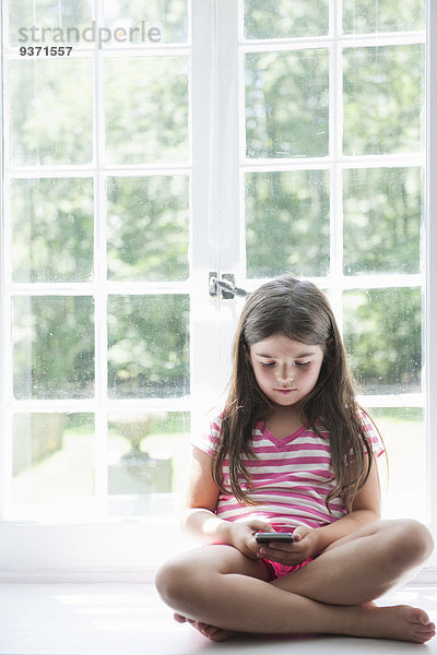 Ein Mädchen sitzt spielend mit einem Smartphone in der Hand.