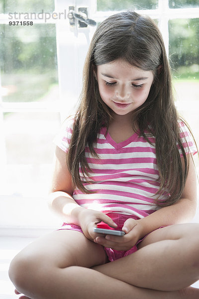 Ein Mädchen sitzt spielend mit einem Smartphone in der Hand.