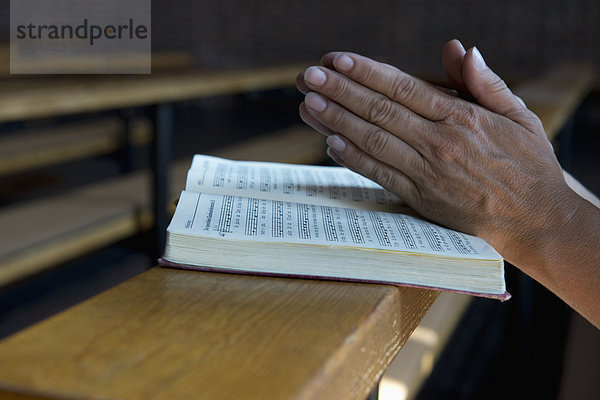 Betende Hände auf einem Gesangbuch in der Kirche