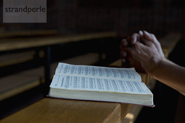 Betende Hände auf einem Gesangbuch in der Kirche