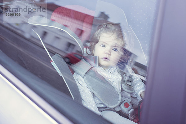 Kleines Mädchen im Autositz sitzend  durch das Autofenster blickend