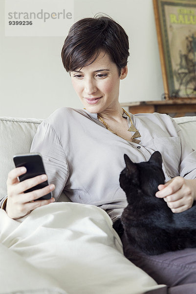 Frau auf dem Sofa sitzend mit Katze auf dem Schoß  mit Smartphone