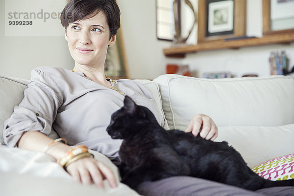 Frau entspannt auf dem Sofa mit Katze auf dem Schoß