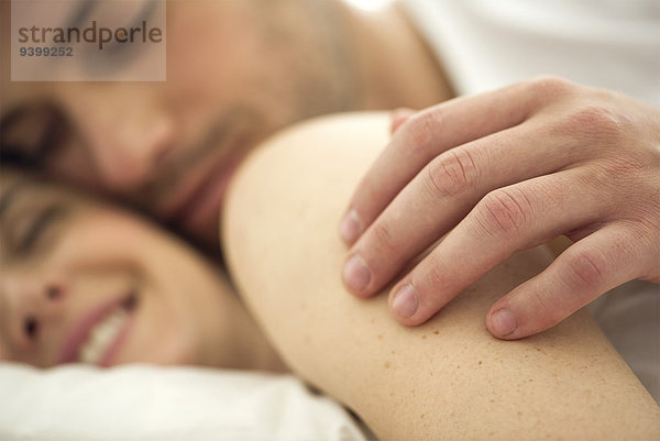 Kuscheln im Bett  die Hand des Mannes auf der Schulter der Frau  Nahaufnahme