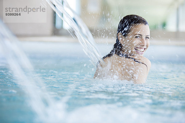 Frau entspannt sich unter dem Springbrunnen im Schwimmbad