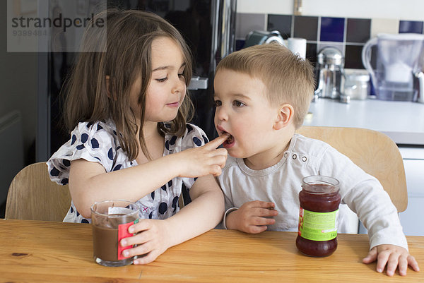 Junge Geschwister schmecken den Inhalt von Gläsern mit den Fingern.