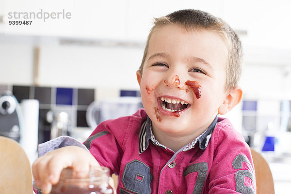 Kleiner Junge mit Marmelade im Gesicht lacht.
