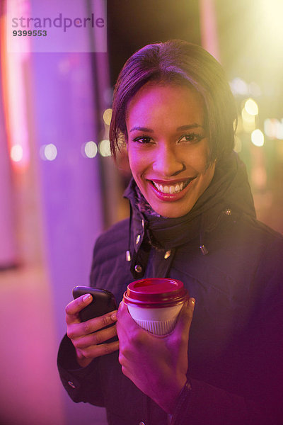 Frau auf der Stadtstraße mit Kaffee und Handy bei Nacht