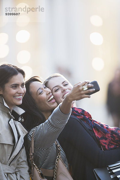 Freunde sprechen Bild mit Handy zusammen in der Stadt Straße