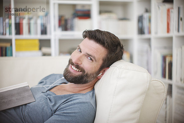 Lächelnder Mann beim Musikhören auf dem Sofa