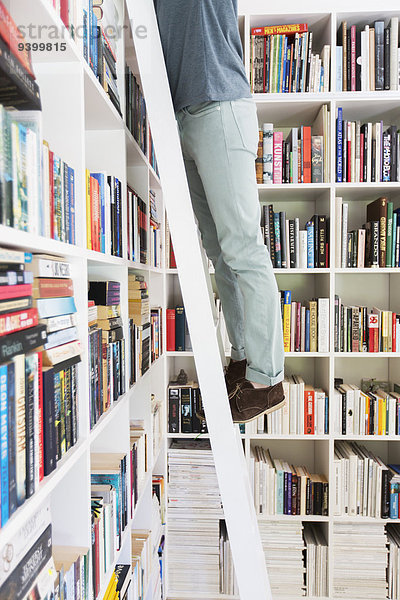 Mann steht auf Leiter  um Bücher in der Bibliothek zu erreichen