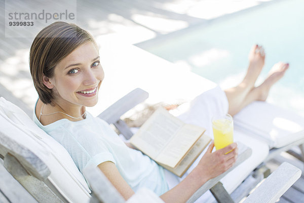Hochwinkelansicht der Frau beim Lesen und Trinken von Saft am Schwimmbad