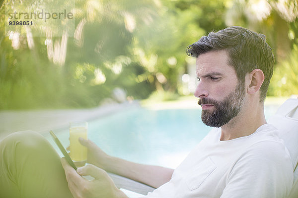 Mann mit digitaler Tablette und Trinksaft im Schwimmbad