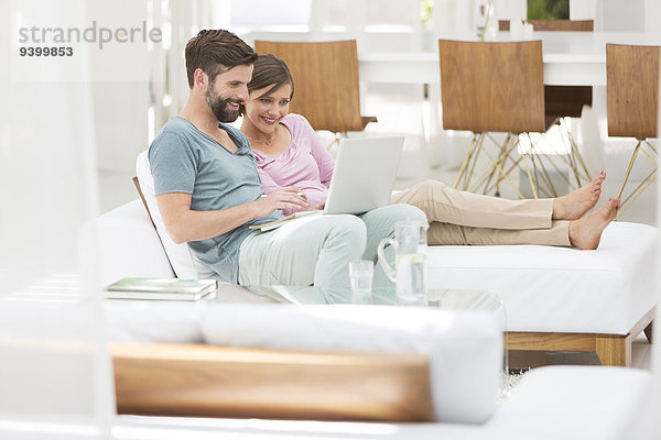 Paar mit Laptop zusammen auf der Liege im modernen Wohnzimmer