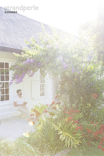 Mann auf der Veranda bewundert Blumen im Hinterhof