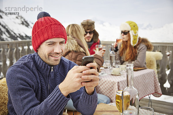 Mann mit Handy auf dem verschneiten Balkon