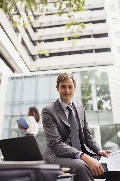 Geschäftsmann  der auf einer Bank außerhalb des Bürogebäudes arbeitet