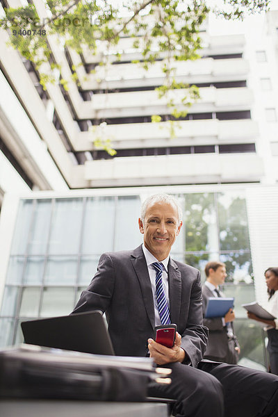 Geschäftsmann  der auf einer Bank außerhalb des Bürogebäudes arbeitet