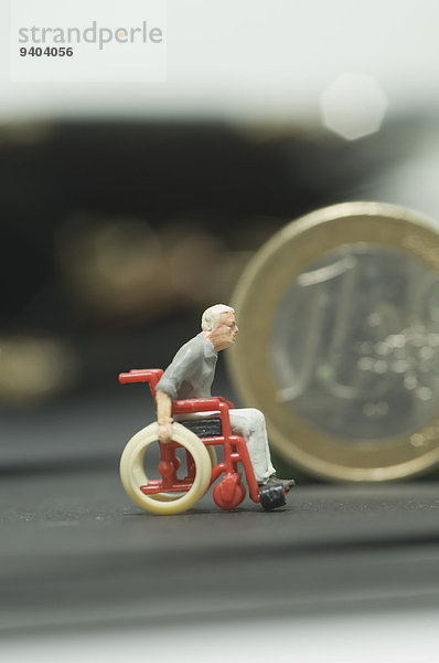 Miniatur-Figur im Rollstuhl und Euromünze