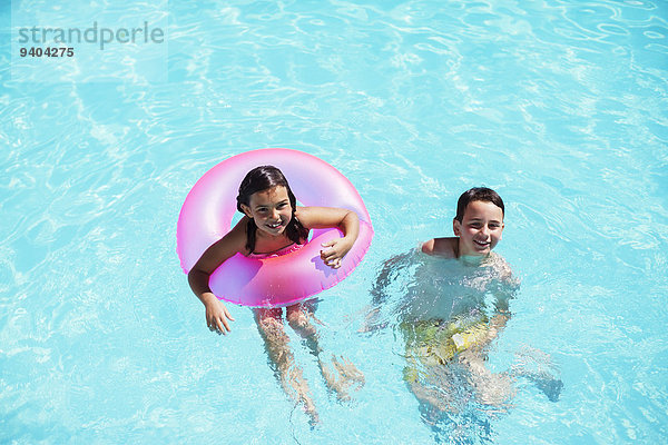 Portrait von Bruder und Schwester mit rosa aufblasbarem Ring im Schwimmbad