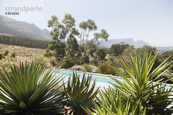 Schwimmbad mit Aloe-Pflanzen im Vordergrund in hügeliger Landschaft