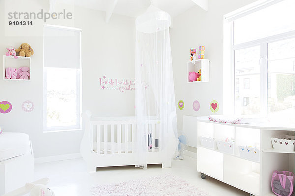 Weiße Krippe mit Tülldach im pastellfarbenen Babyzimmer