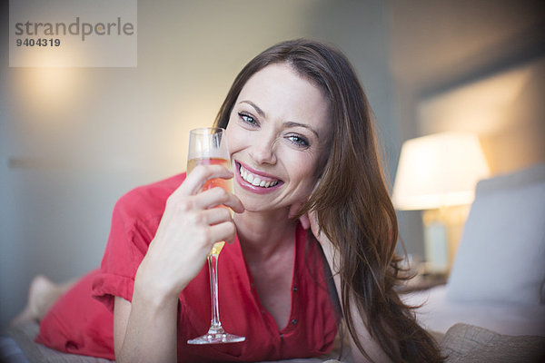 Porträt einer lächelnden Frau auf dem Bett liegend mit Champagnerflöte