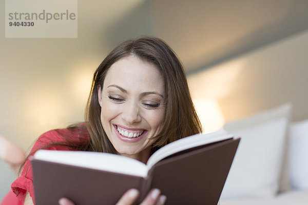 Lächelnde Frau liest Buch im Schlafzimmer