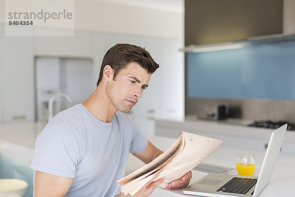 Mann liest Zeitung in der modernen Küche  Laptop und Orangensaft auf der Theke