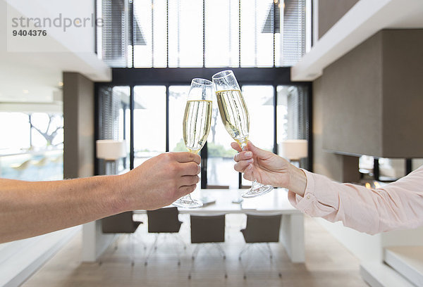 Hände des Paares  das Toast mit Champagnerflöten im modernen Speisesaal erhebt.