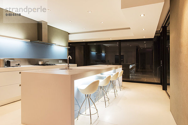 Moderne weiße Küche mit Kücheninsel und nachts beleuchteten Hockern