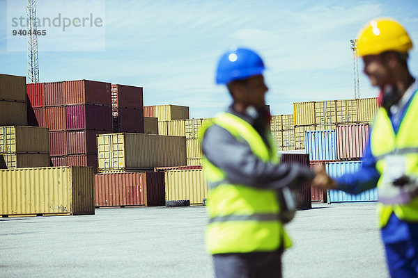 Arbeiter und Geschäftsmann beim Händeschütteln in der Nähe von Frachtcontainern