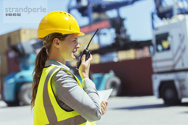 Geschäftsfrau mit Walkie-Talkie in der Nähe von Frachtcontainern und Lastwagen