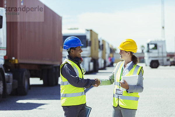 Arbeiter und Geschäftsfrau beim Händeschütteln in der Nähe von Lastwagen und Frachtcontainern