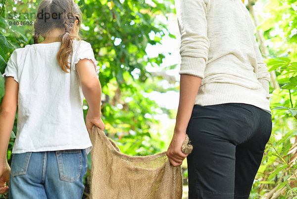 Rückansicht der Frau und des Mädchens mit Sackleinen durch den Garten