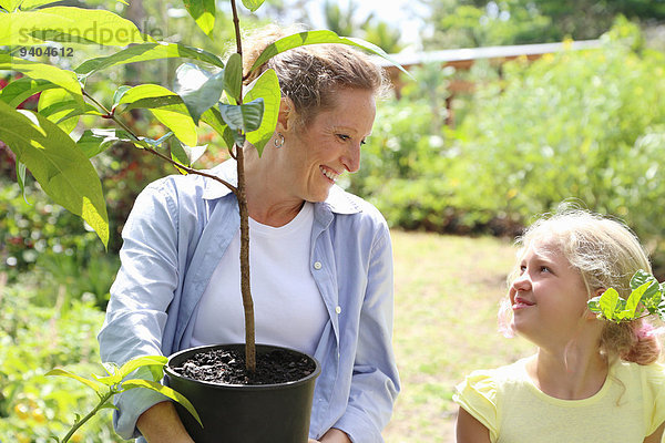 Frau und Mädchen mit Baumsetzling im sonnigen Garten