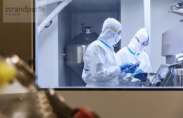 Wissenschaftler in sauberen Anzügen mit digitalen Tabletten im Laborversuch