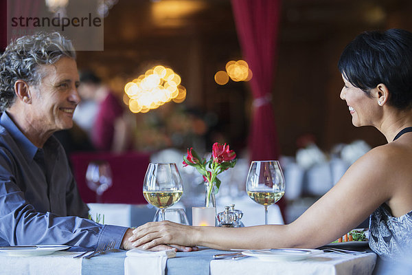 Ein reifes Paar sitzt von Angesicht zu Angesicht und hält die Hände am Restauranttisch.