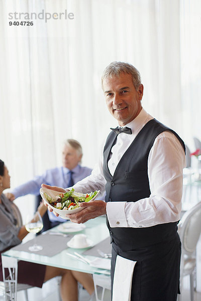 Porträt des Kellners mit Salatschüssel  Menschen am Tisch im Hintergrund