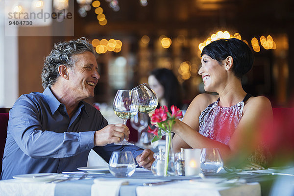 Lächelndes reifes Paar  das mit Weißwein am Restauranttisch anstößt.
