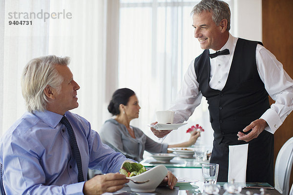 Kellner serviert eine Tasse Kaffee an einen reifen Mann  der am Tisch im Restaurant sitzt.