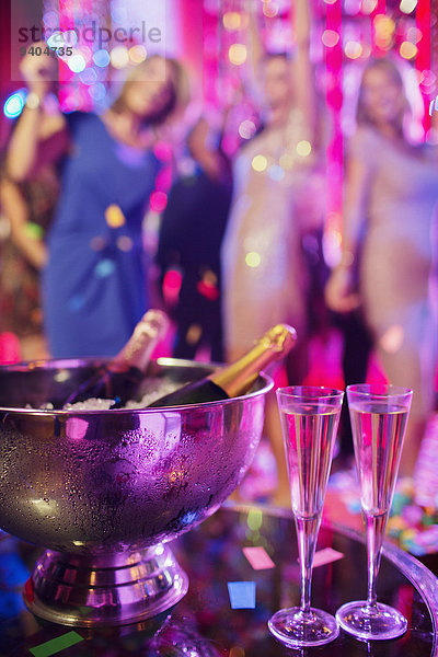 Champagnerflaschen im Eiskübel und Champagnerflöten im Nachtclub  Menschen tanzen im Hintergrund