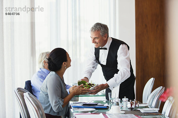 Lächelnder Kellner serviert Salat an eine Frau  die am Tisch im Restaurant sitzt.